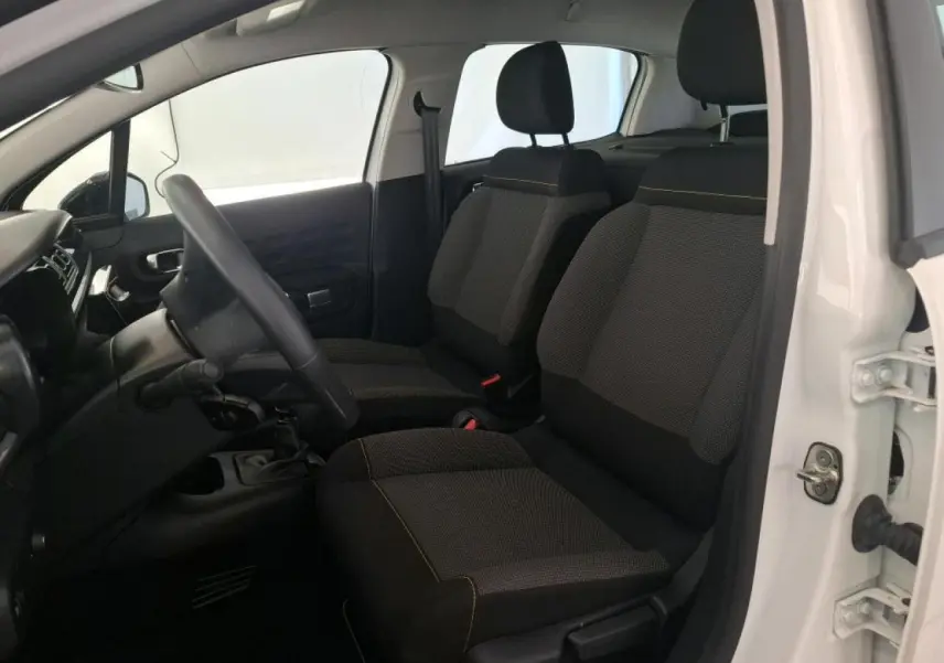 Vue intérieure côté conducteur d'une Citroën C3 blanche 2023 avec sièges tissu gris et volant réglable.