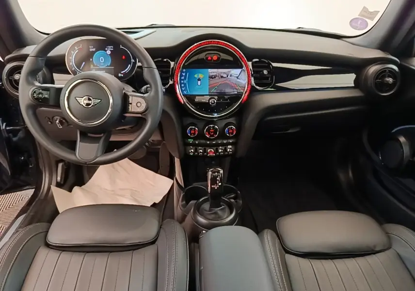 Vue intérieure avant de la MINI Cooper Premium Plus 2023, tableau de bord noir avec écran central rond et volant cuir multifonctions.