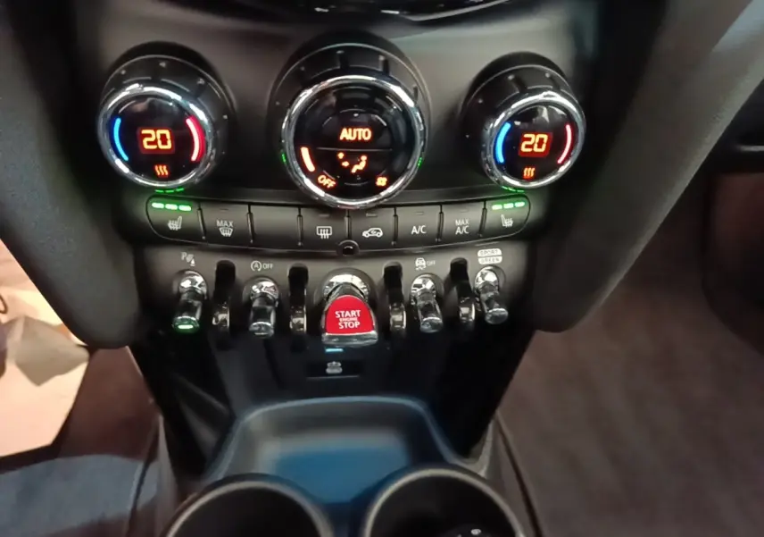 Vue rapprochée du tableau de bord central de la MINI Cooper Edition Premium Plus 2023 avec commandes climatisation et bouton start/stop rouge.