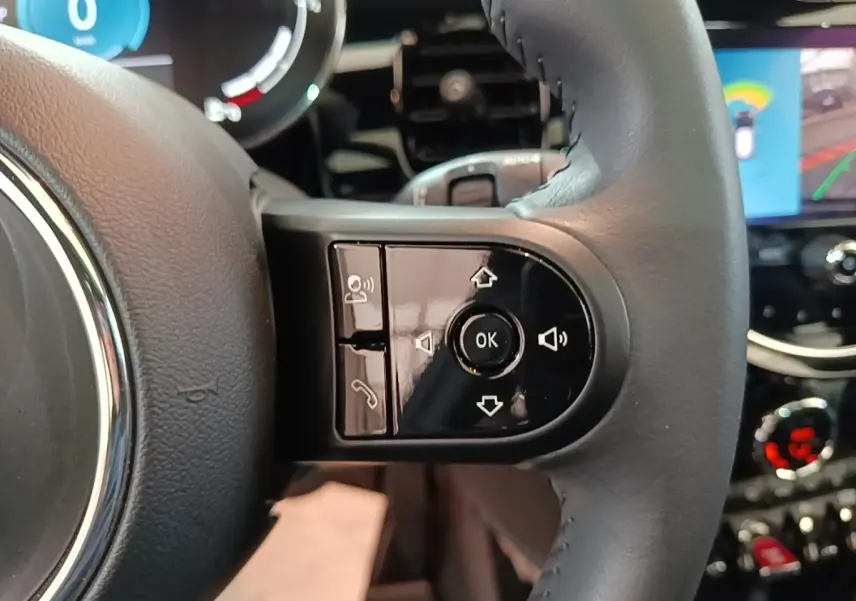 Gros plan sur la partie droite du volant cuir noir de la MINI Cooper 2023 avec commandes multifonctions et tableau de bord numérique.