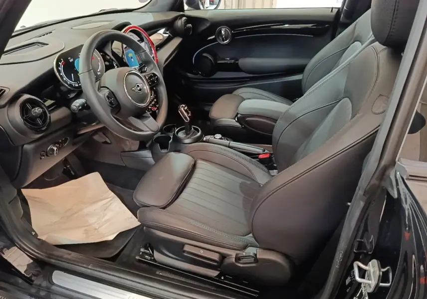 Intérieur noir de la MINI Cooper Premium Plus 2023 vu côté conducteur, avec sièges sport et volant cuir multifonctions.