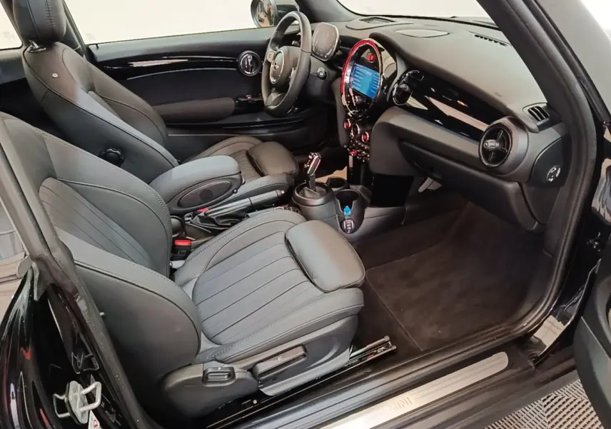 Intérieur noir de la MINI Cooper Premium Plus 2023 vu côté conducteur, avec tableau de bord digital et sièges sport cuir.