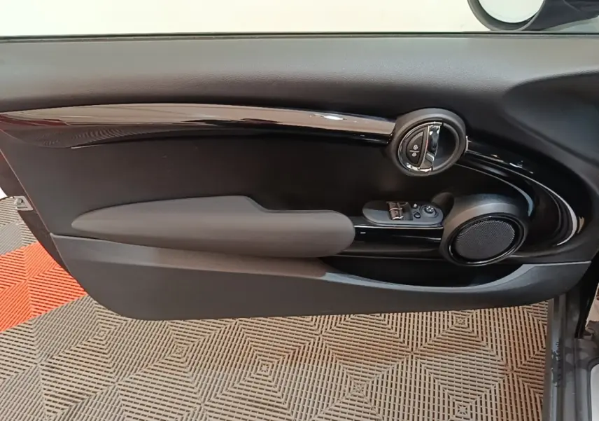 Gros plan sur la porte intérieure côté conducteur de la MINI Cooper noire, avec commandes de vitres et haut-parleur rond.