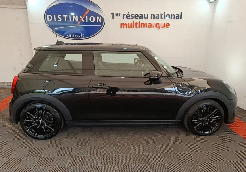 Profil côté gauche d'une MINI Cooper Edition Premium Plus noire 3 portes avec jantes noires brillantes en intérieur showroom.