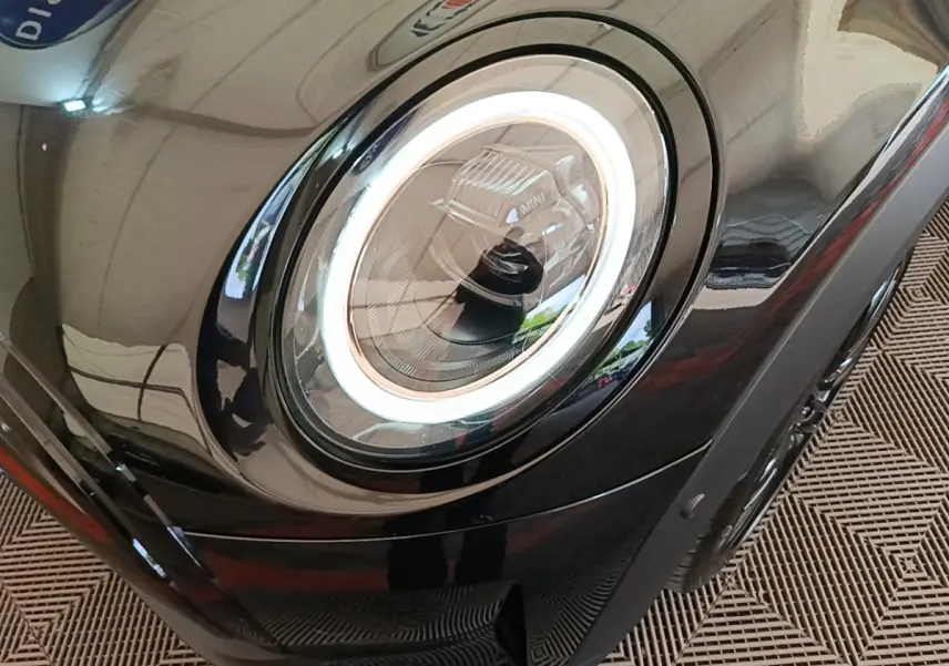 Gros plan sur le phare avant gauche LED d’une MINI Cooper Edition Premium Plus noire, soulignant son design circulaire moderne.