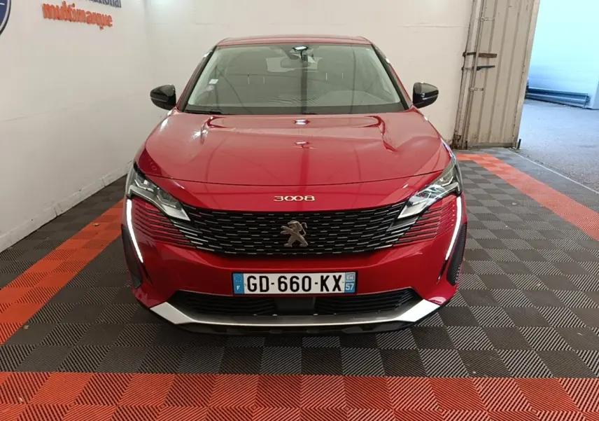 Vue avant frontale d'un Peugeot 3008 rouge avec calandre noire et feux LED verticaux allumés dans un garage.