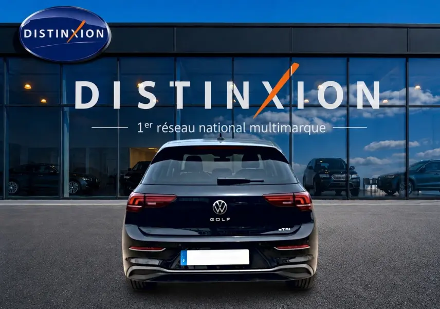 Vue arrière d'une Volkswagen Golf noire 2026 avec feux arrière LED, garée devant une vitrine Distinxion.