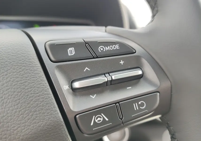 Gros plan sur les commandes multifonctions noires du volant cuir côté gauche du Hyundai Kona électrique gris métallisé 2025.