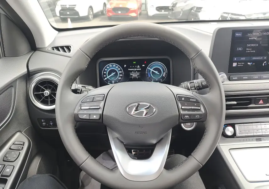 Vue intérieure centrée sur le volant cuir gris et le tableau de bord numérique du Hyundai Kona Electric 2025.