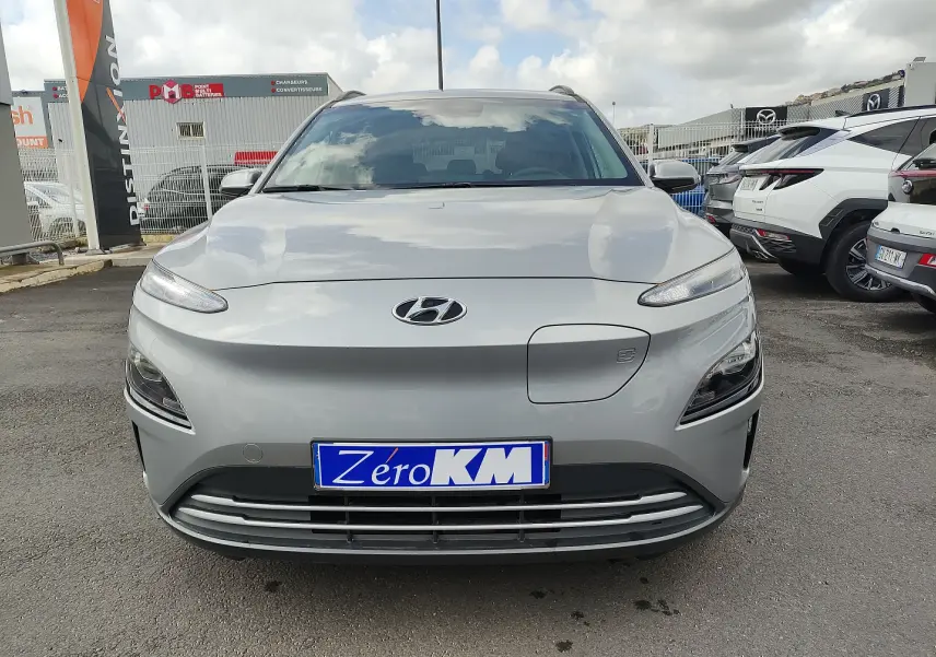 Vue avant d'un Hyundai Kona Electric gris métallisé avec prise de recharge visible sur le capot, en extérieur.