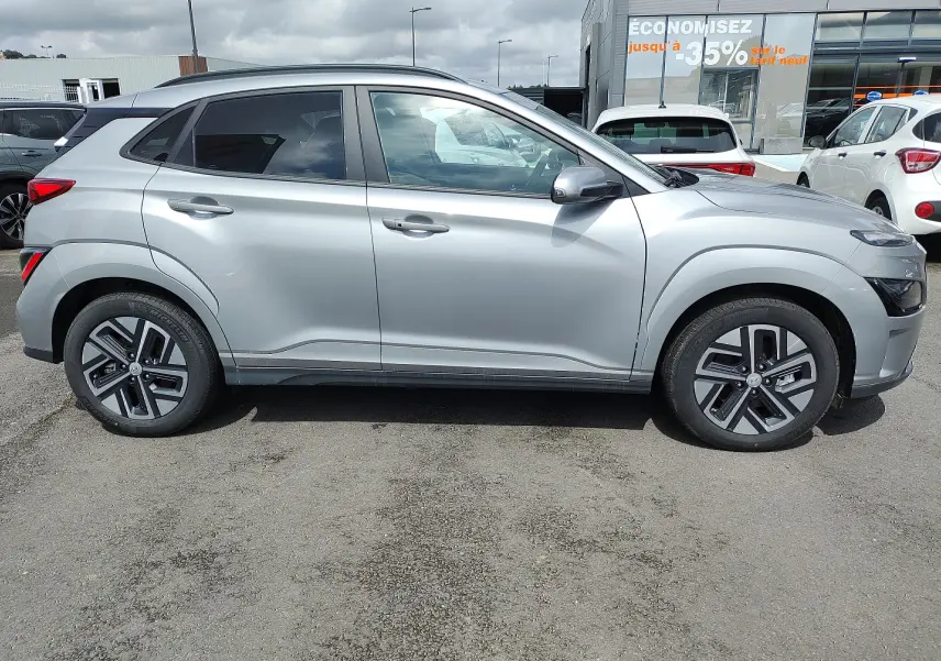Vue de profil côté gauche d'un Hyundai Kona électrique gris métallisé avec jantes alliage 17 pouces et vitres arrière surteintées.