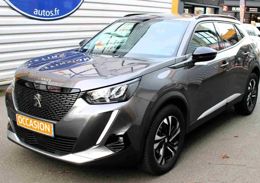 Peugeot 2008 gris platinium en 3/4 avant droit, avec jantes noires et calandre imposante, stationné en extérieur.