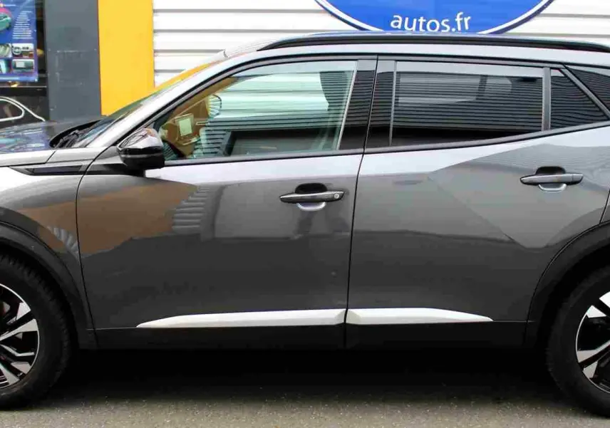 Profil droit du Peugeot 2008 gris platinium 2022 avec jantes noires et détails chromés sur les bas de portes.