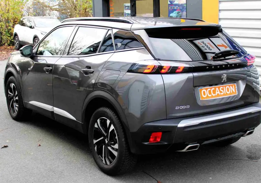 Peugeot 2008 gris platinium vue 3/4 arrière droit, feux arrière allumés et jantes noires bicolores.