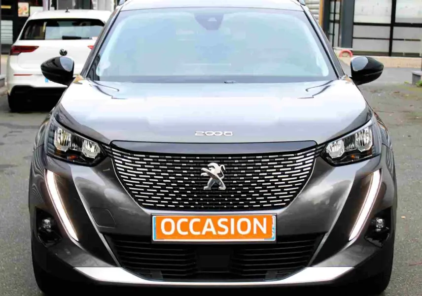 Vue frontale d'un Peugeot 2008 gris platinium avec calandre distinctive et feux LED en forme de griffes allumés.