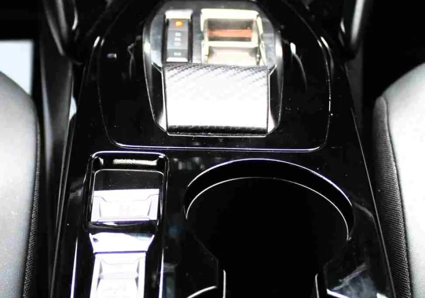 Gros plan sur la console centrale noire brillante du Peugeot 2008 II, avec levier de vitesse et porte-gobelets visibles.