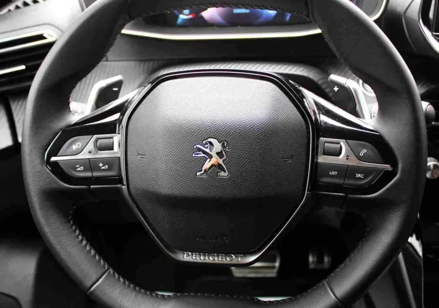 Gros plan sur le volant noir du Peugeot 2008 gris platinium, avec commandes intégrées et logo lion central.