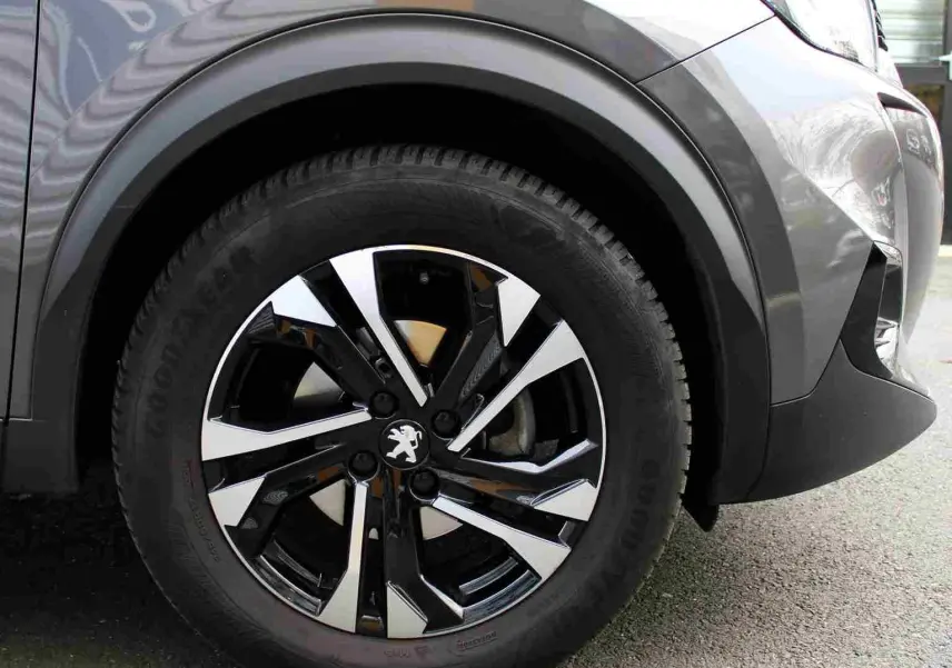 Gros plan sur la roue avant gauche du Peugeot 2008 gris platinium avec jante alliage bicolore au design moderne.