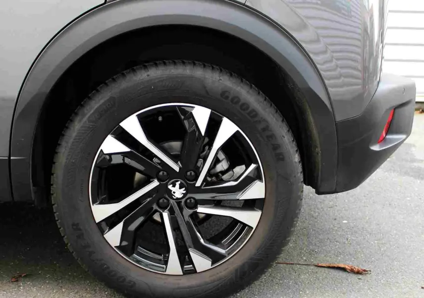 Gros plan sur la roue arrière droite du Peugeot 2008 gris platinium avec jante alliage bicolore et logo lion central.