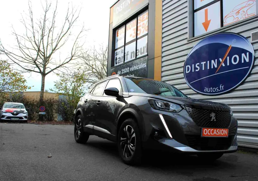 Peugeot 2008 gris platinium vue 3/4 avant droit, garée devant un bâtiment avec panneau Distinxion.