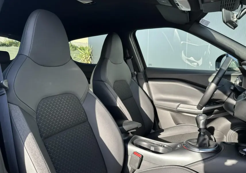 Vue intérieure côté droit du Nissan Juke 2025 noir, montrant les sièges avant en cuir et la console centrale avec levier de vitesses manuel.