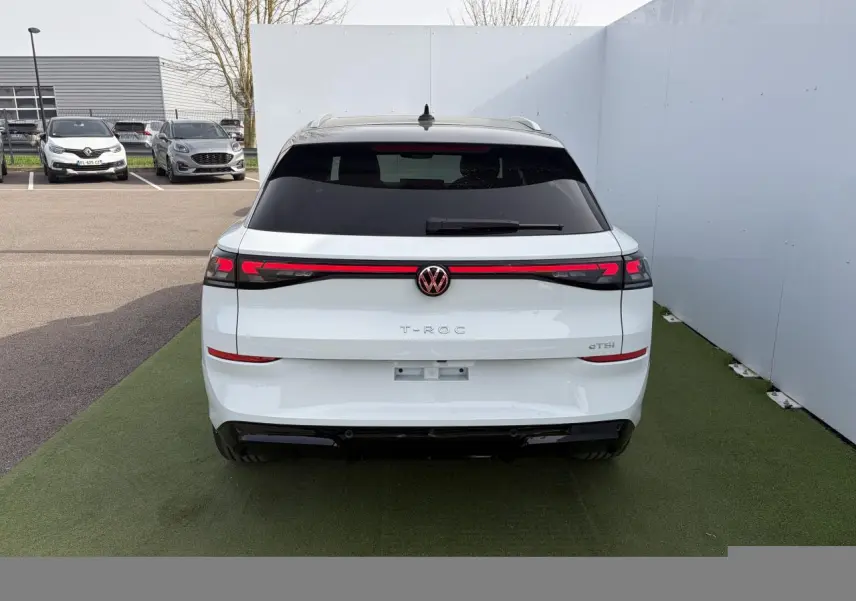 Vue arrière d'un Volkswagen T-Roc blanc pur avec toit noir et bandeau lumineux rouge intégrant le logo VW rétroéclairé.