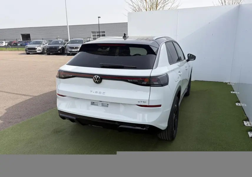 Volkswagen T-Roc blanc pur toit noir vu 3/4 arrière droit, feux arrière LED et logo VW rétroéclairé.