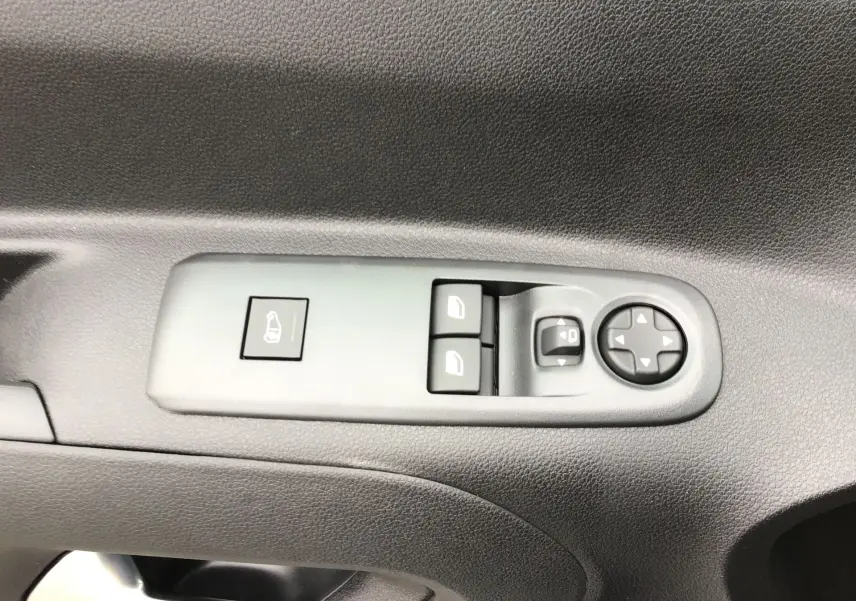 Gros plan sur les commandes de lève-vitres et rétroviseurs électriques sur la porte intérieure d’un Peugeot Partner blanc.