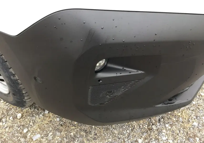 Gros plan sur le pare-chocs avant droit noir mat du Peugeot Partner blanc, avec antibrouillard et capteur de stationnement.