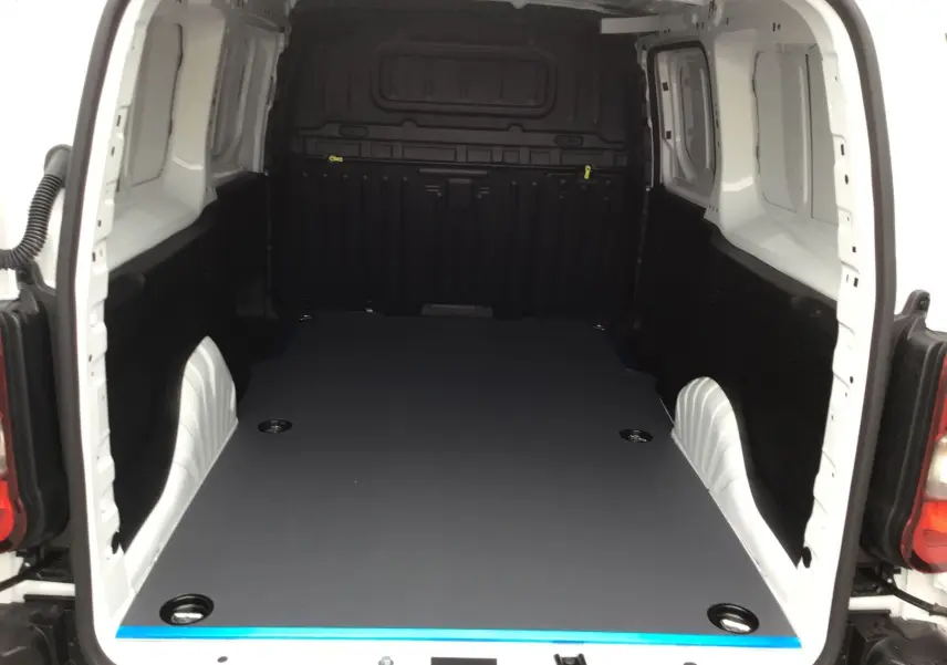 Vue intérieure arrière du Peugeot Partner blanc 2026, montrant l'espace de chargement avec plancher antidérapant gris et renforts noirs.