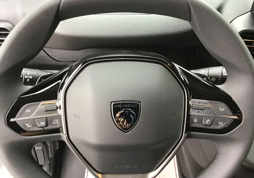 Gros plan sur le volant noir du Peugeot Partner blanc 2026 avec commandes intégrées et logo lion central.