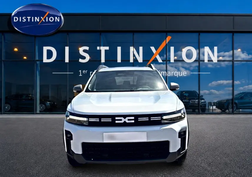 Vue de face du Dacia Bigster blanc 2026 avec calandre noire et phares LED fins devant une vitrine Distinxion.