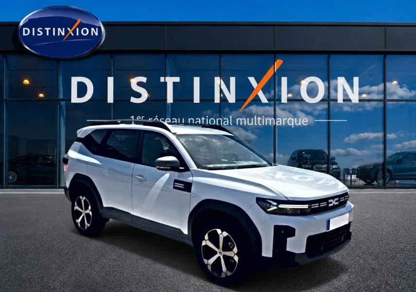 Vue 3/4 avant droit du SUV blanc Dacia Bigster 2026 avec barres de toit et jantes alu distinctives, devant un showroom Distinxion.
