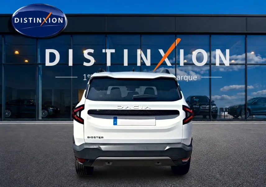 Vue arrière d'un Dacia Bigster blanc avec feux arrière LED et barres de toit, devant une vitrine Distinxion.