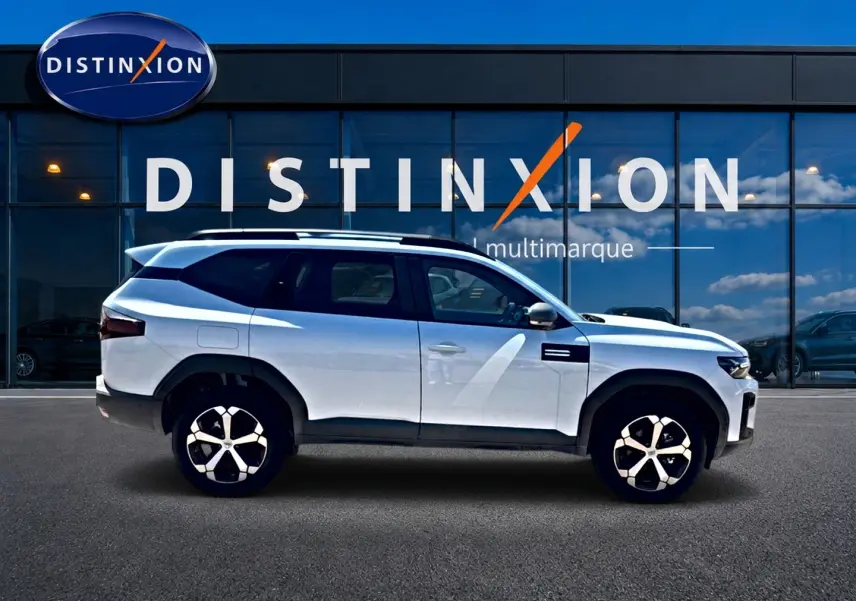 Vue latérale droite du SUV Dacia Bigster blanc 2026 avec jantes alu et barres de toit noires visibles.