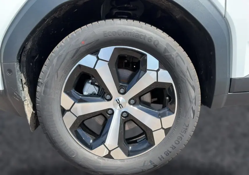 Gros plan sur la roue avant gauche du Dacia Bigster blanc, jante alliage bicolore au design hexagonal.