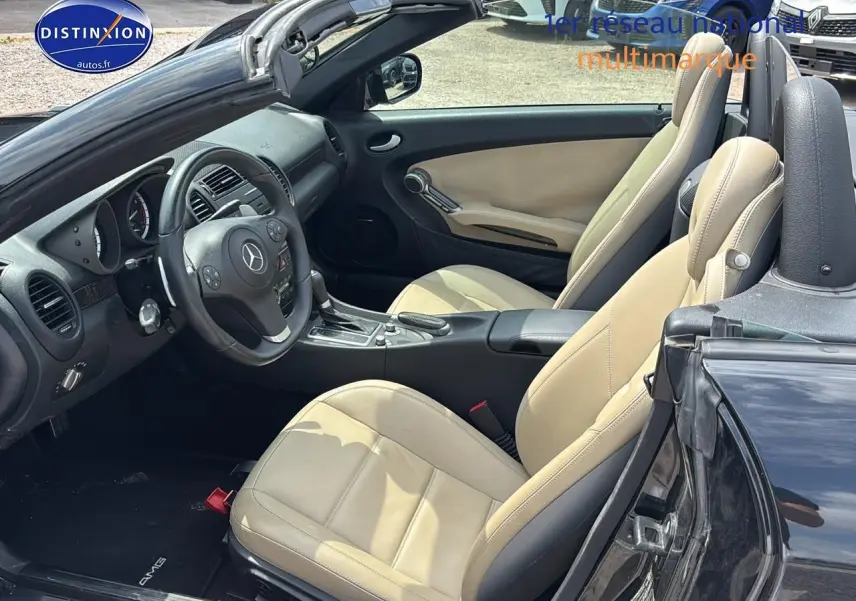 Intérieur beige clair vu côté conducteur d'une Mercedes SLK 55 AMG noire cabriolet avec volant multifonction et boîte auto.