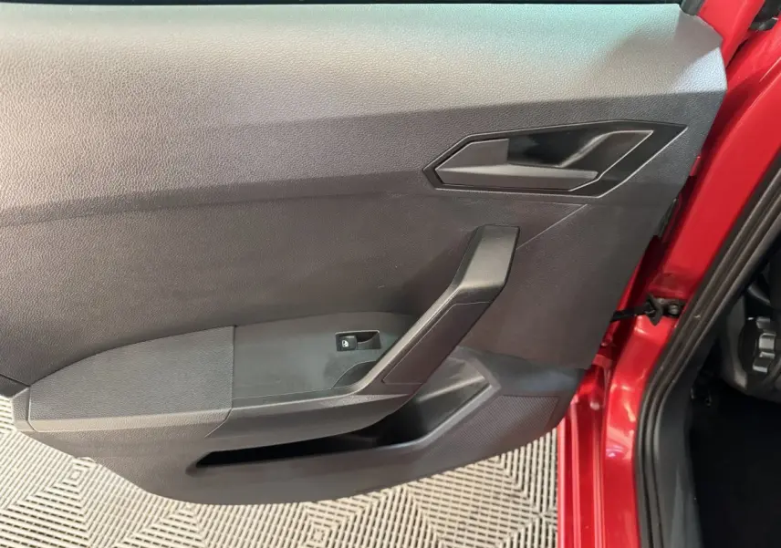 Vue rapprochée de la porte avant gauche rouge de la SEAT IBIZA 1.0 TSI 110 FR avec poignée et commande de vitre noire.