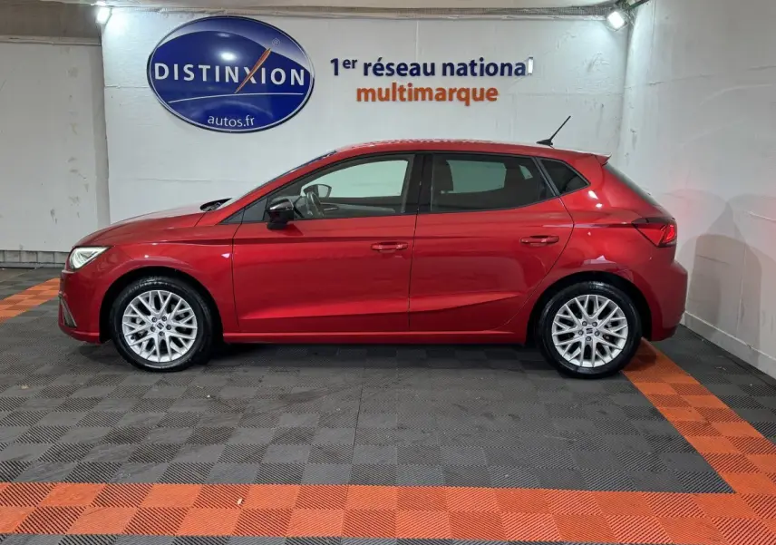 Profil côté gauche d'une SEAT IBIZA 1.0 TSI 110 FR rouge, en intérieur sur sol à damiers gris et orange.