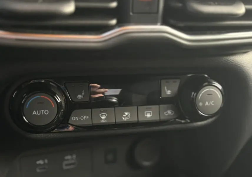 Gros plan sur la console centrale noire du Nissan Juke 2025 montrant les commandes de climatisation automatique et sièges chauffants.