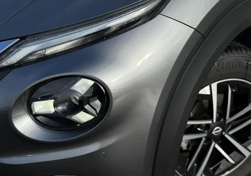 Gros plan sur le phare avant droit et la jante alliage diamantée du Nissan Juke 2025 gris foncé.