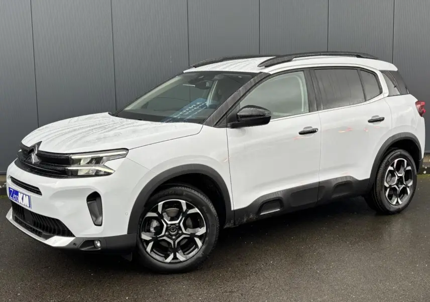 Vue 3/4 avant droite d’un Citroën C5 Aircross blanc Okénite avec jantes alliage bi-ton et barres de toit noires.