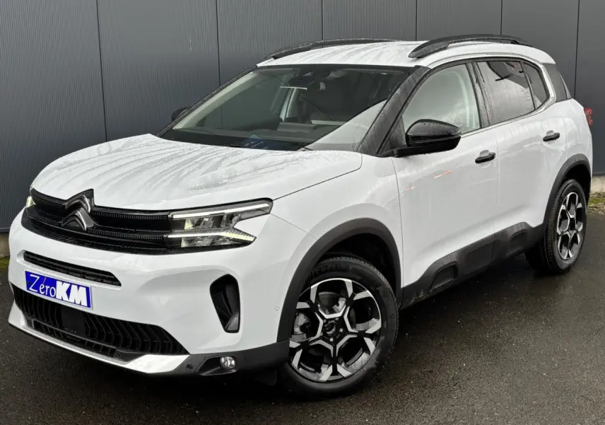 Vue 3/4 avant droit d'un Citroën C5 Aircross blanc Okénite avec jantes alliage 18'' bi-ton et barres de toit noires.