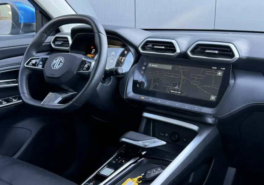 Vue intérieure côté conducteur du MG ZS Hybrid+ 2025, avec tableau de bord noir et écran tactile de navigation.