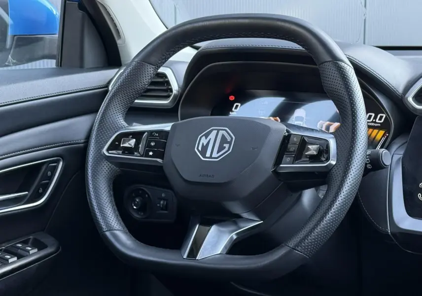 Vue rapprochée du volant en cuir noir perforé du MG ZS 1.5 Hybrid+ 197 Luxury avec tableau de bord numérique visible.