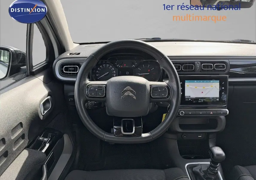 Vue intérieure frontale du tableau de bord noir d'une Citroën C3 blanche 2021 avec volant multifonction et boîte manuelle.