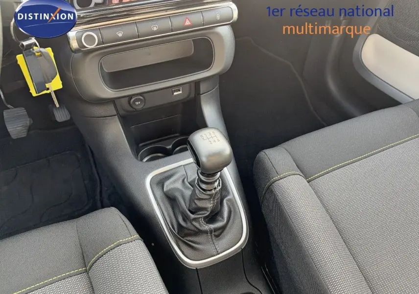 Vue intérieure centrée sur la console centrale et levier de vitesse manuel d'une Citroën C3 2021 avec sièges gris et surpiqûres jaunes.