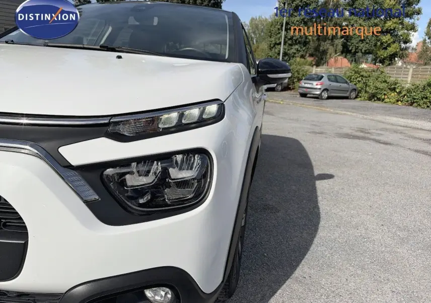 Gros plan sur l’avant droit d’une Citroën C3 blanche 2021, mettant en valeur ses phares LED distinctifs et le rétroviseur noir.