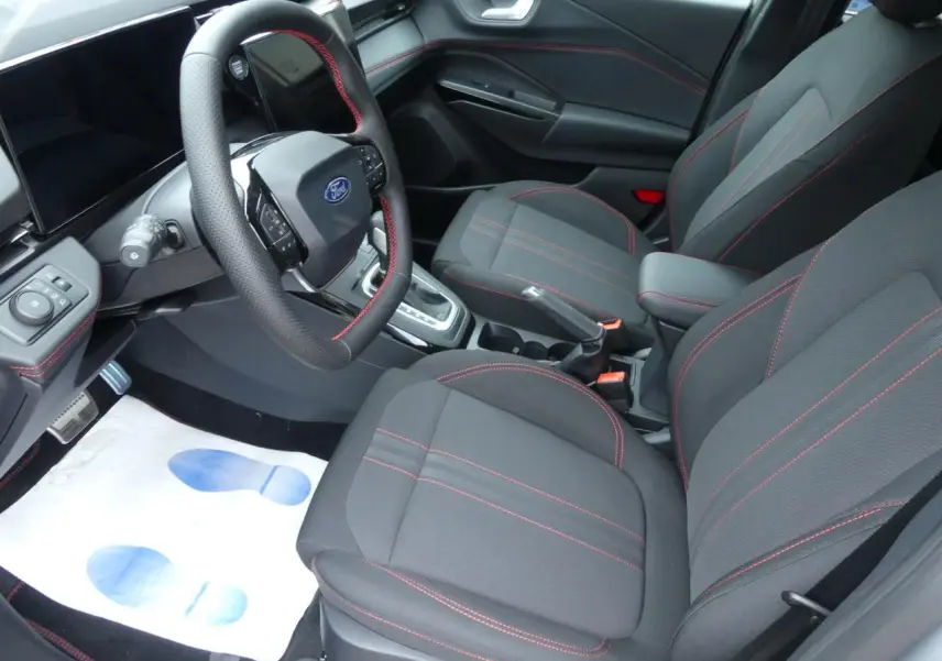 Intérieur avant du Ford Puma 2025 avec sièges tissu noirs à surpiqûres rouges et volant sport multifonction.