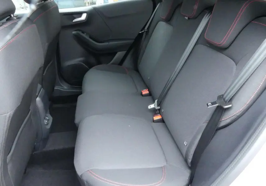 Vue intérieure côté arrière droit du Ford Puma 2025, sièges arrière en tissu gris avec surpiqûres rouges et ceintures de sécurité.